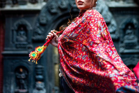 Person in a vibrant red and orange patterned outfit holding a decorative object against a dark, ornate background.