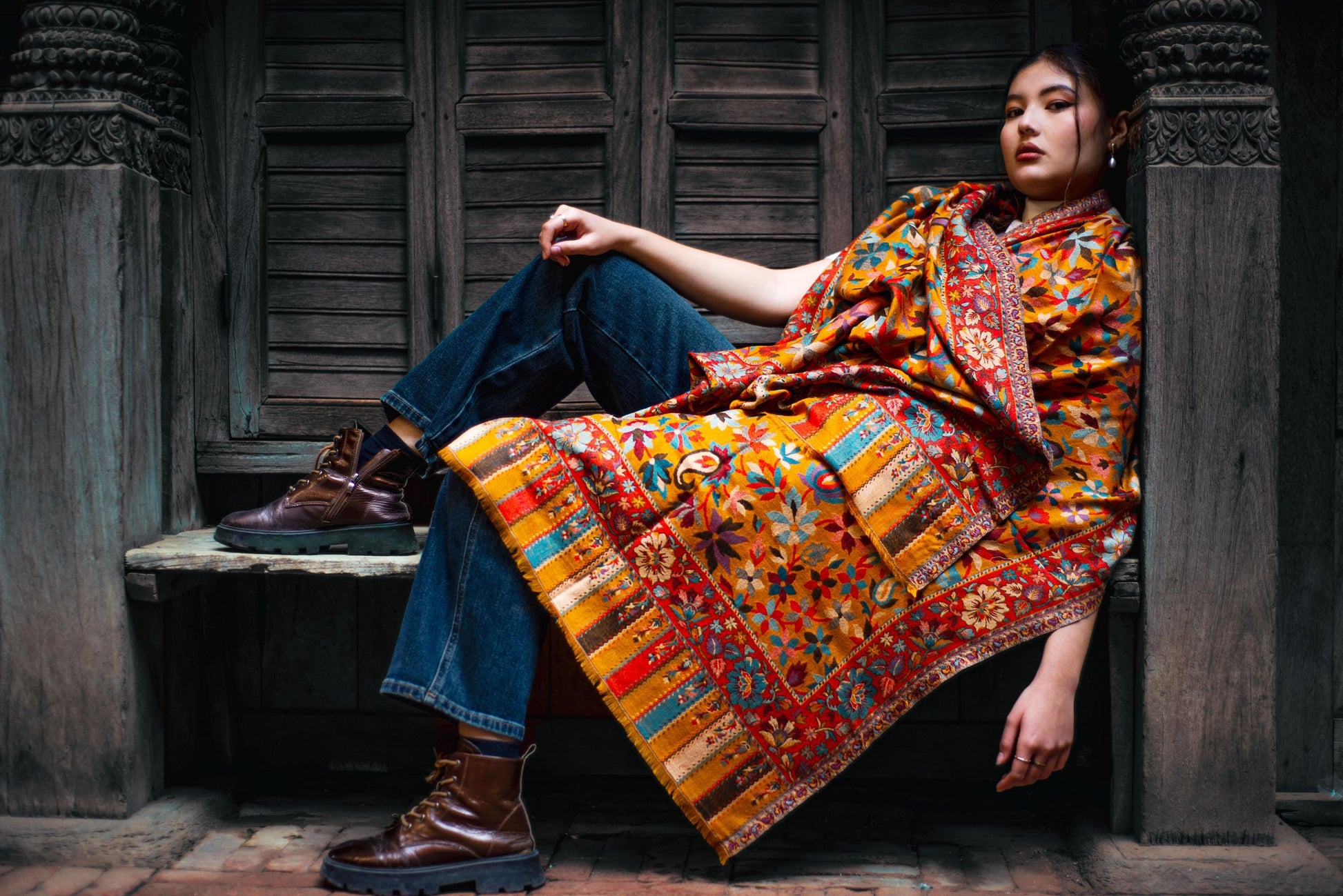 Woman wearing a colorful patterned shawl sitting in a rustic setting.