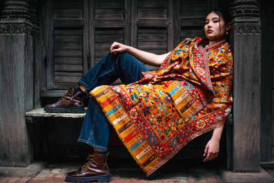 Woman wearing a colorful patterned shawl sitting in a rustic setting.