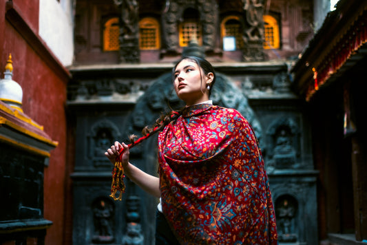 Woman in a red patterned dress holding prayer beads in front of a temple.